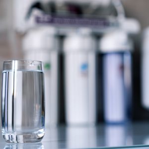 Pure water in glass and water filters on the blurred background. Household filtration system.